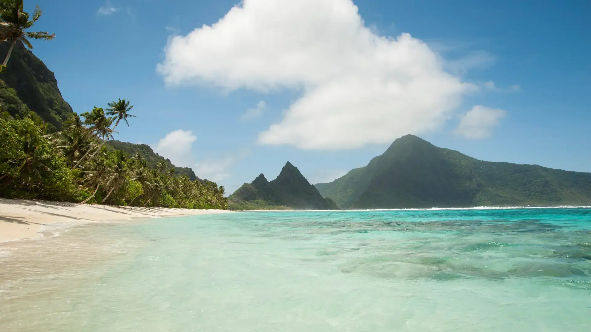 White sand and turquoise water on Ofu Island, with the peaks of Olosega in the distance.