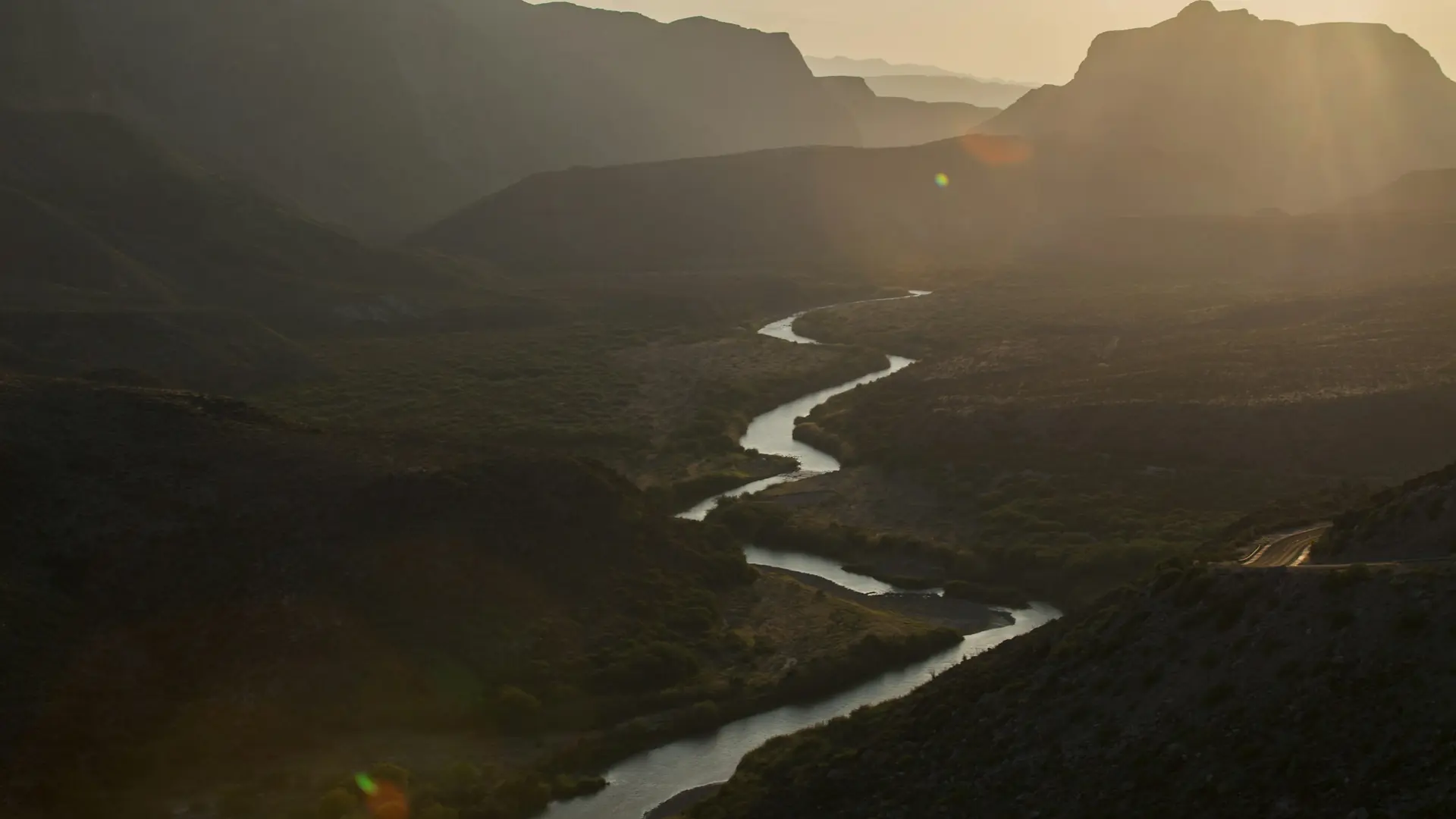 A winding river flows through a mountain valley at sunset