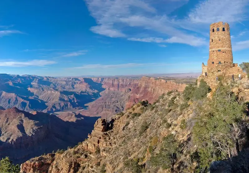 A cylindrical, stone tower, 70 feet (21 m) is on the edge of a vast, mile-deep canyon