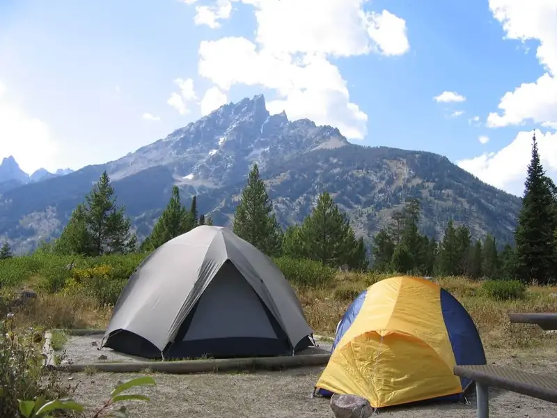 Two tents in a campground in front of a mountain.