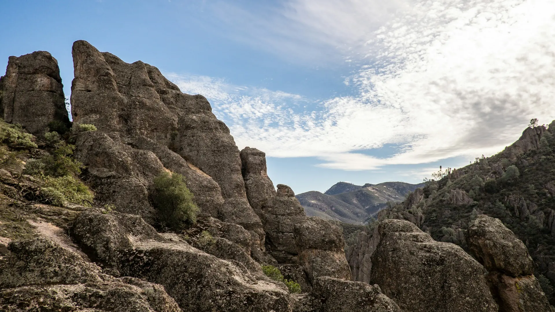 Rock spires and a mountain valley beneath a cloud-streaked sky in Pinnacles National Park.