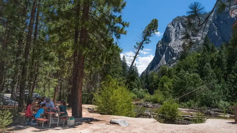 A family sits at a picnic table by the river.