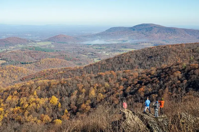 Visitors stand on a rocky outcrop overlooking the receding mountains.
