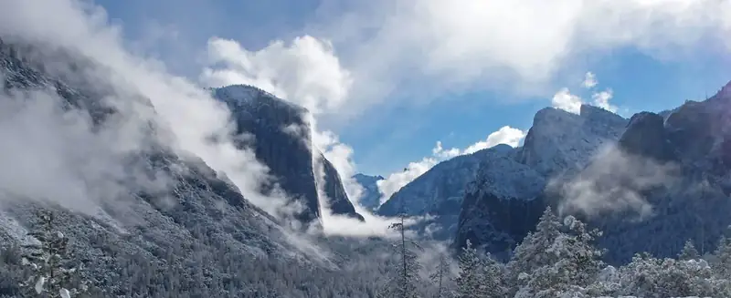 El Capitan on left, Cathedral Rocks on the right, all covered in snow, low clouds and sun