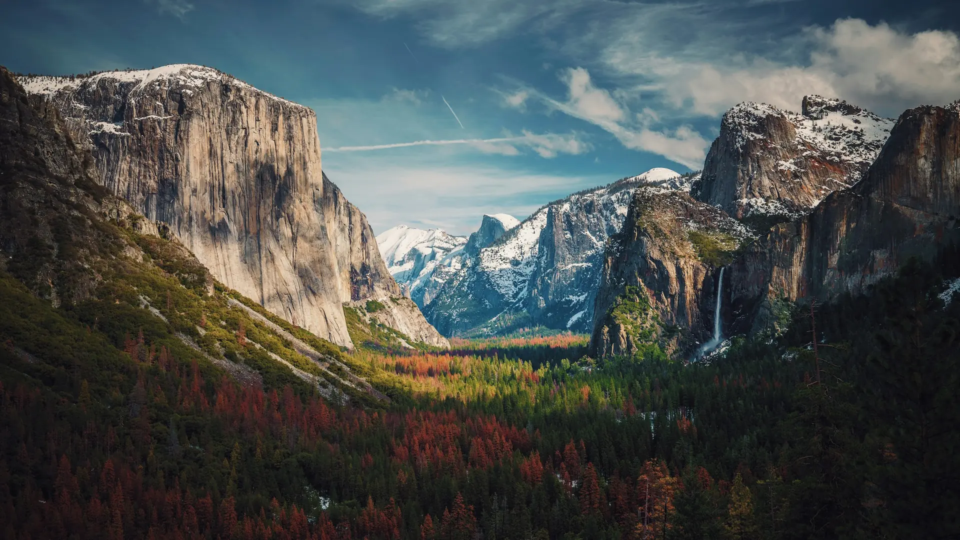 Snow-dusted granite cliffs and a waterfall above a forest in Yosemite National Park