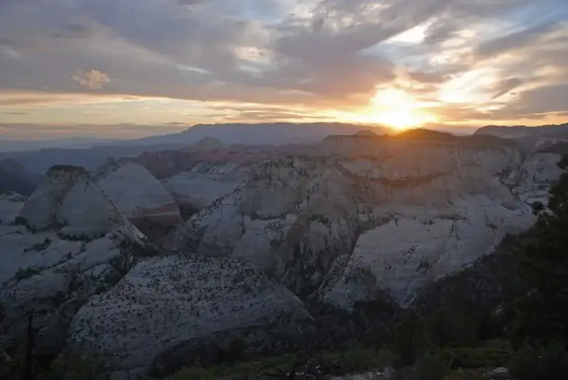 Sunset behind distant mountains, with a maze of canyons in the foreground.